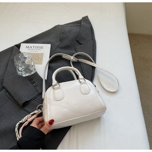 Detail showing white leather pillow bag with adjustable strap and braided charm accent