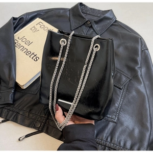 Detail of black glossy bucket bag featuring chunky silver chains and pleated texture