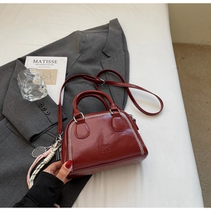Detail view of red leather pillow bag with white stitching and tennis racket charm accessory