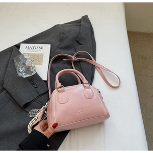 Detail of pink pillow bag with white stitching and tennis racket charm on grey blazer