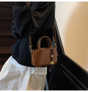 Bruine gepolijste lederen mini Boston tas met gouden hanger gedragen door model