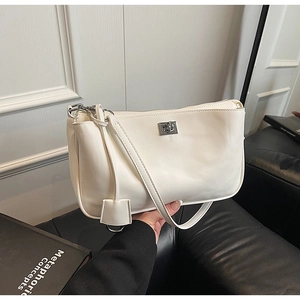 Detail of minimalist beige leather shoulder bag with silver metal plate and side pendant
