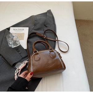 Detail of dark brown leather pillow bag with white stitching and decorative tennis charm