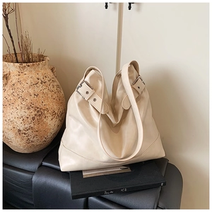 Detail of a cream faux leather tote bag with silver buckle on a black leather bench