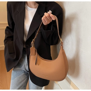 Detail of brown pleated crescent shoulder bag featuring woven texture and fashion tag