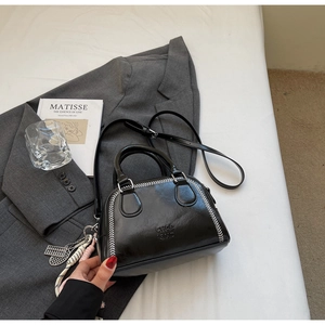 Detail of black leather pillow bag with white contrast stitching and unique metal charms
