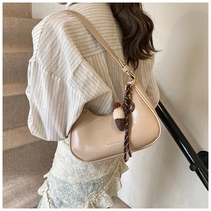 Sac hobo demi-lune beige avec pendentif gland et ruban porté par un modèle
