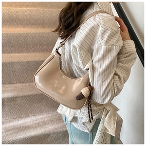 Détail du sac hobo montrant le cuir verni beige et un charm de noud en peluche