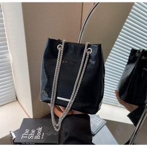 Close-up of black glossy leather bucket bag with silver woven chain straps and metallic bar