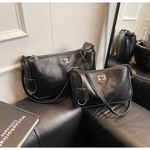 Detail of two black leather shoulder bags with silver square locks on a leather sofa