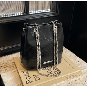 Detail of glossy black leather bucket bag with silver chain straps and retro texture