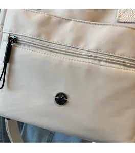 Detail of cream nylon tote bag featuring a zipper pocket and round M FASHION metal logo