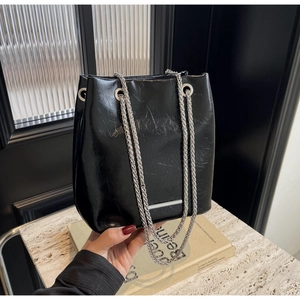 Close-up of black glossy leather bucket bag with silver metal chain and fine textures