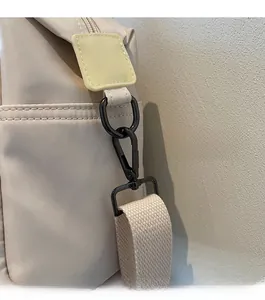 Detail of high-gloss black metal hardware and woven strap on a beige tote bag