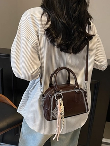 Retro dark brown patent leather pillow bag with white stitching and woven pendant