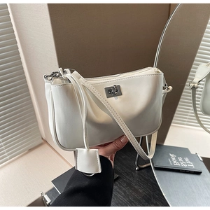Detail of a creamy white leather shoulder bag featuring a silver metal twist-lock and charm