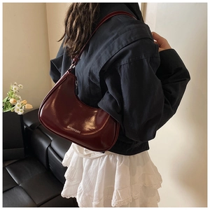 Modèle portant un sac demi-lune bordeaux brillant dans un intérieur élégant