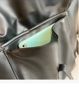 Détail du sac cabas en cuir noir montrant une poche avant contenant une tablette verte