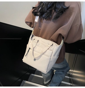 Model wearing a beige nylon crossbody tote bag with adjustable strap in a modern setting