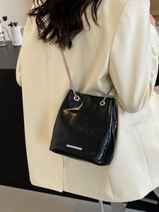 Fashionable black leather bucket bag with silver chain strap worn over the shoulder