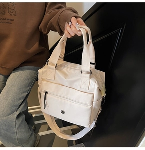 Detail of off-white nylon tote bag showing front zip pocket and sturdy webbing handles