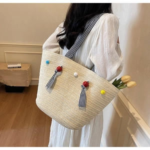 Detail of woven straw tote bag with colorful pom-poms and striped shoulder straps