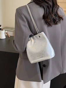 Silver metallic chain bucket bag in pleated texture worn over shoulder with grey suit