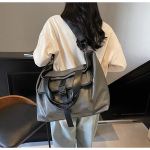 Détail d'un grand cabas vert gris avec sangles en cuir noir et boucle en métal porté à l'épaule