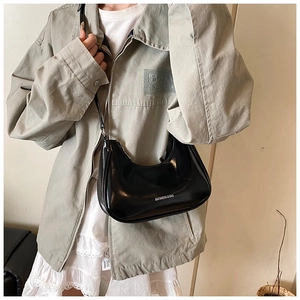 Détail d'un sac hobo en cuir verni noir avec logo argenté porté par un mannequin