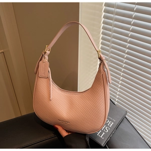Detail of pink woven leather hobo bag with gold hardware and brand tag on a dark desk
