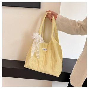 Dettaglio della borsa tote gialla con fiocco in pizzo bianco ed etichetta ricamata LOVE