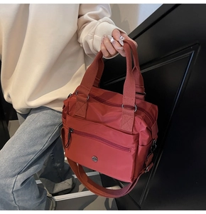 Detail of brick red nylon tote bag featuring multi-pocket design and adjustable strap