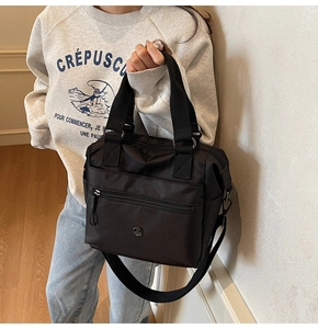 Detail of black nylon tote bag featuring zip pocket, metal logo and adjustable strap