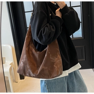 Close-up of a large brown hobo bag with glossy pleated texture on a model's shoulder