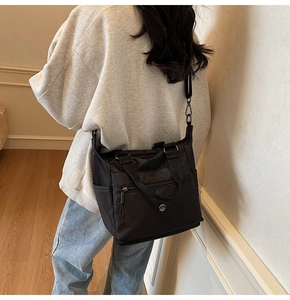 Detail of a large black nylon tote bag with metal M logo shown on a model side view