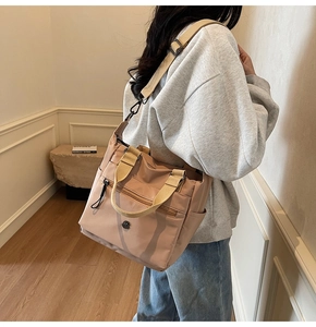 Detail of a dusty pink nylon tote bag showing multiple zipper pockets and beige straps