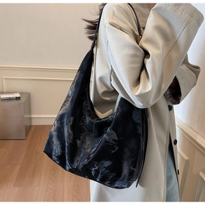 Detail of a large black leather tote with a glossy vintage finish and wide shoulder strap