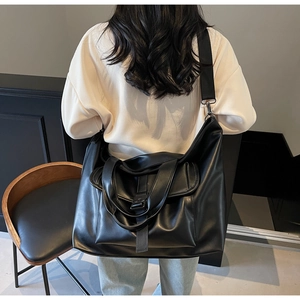 Gros plan d'un grand sac cabas noir en similicuir porté par un mannequin dans un décor épuré