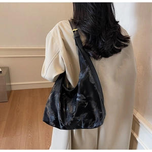 Detail of black glossy hobo bag featuring a wide strap and gold square buckle