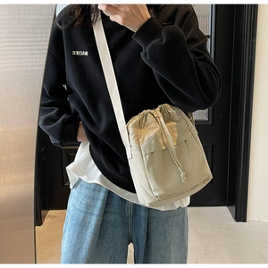 Dettaglio della borsa a secchiello in nylon beige con tracolla in tela e fibbia regolabile