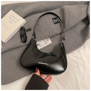 Détail d'un sac hobo en cuir verni noir avec logo BAFANSHA sur un fond texturé gris clair