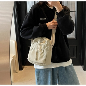 Dettaglio di una borsa a secchiello beige con coulisse, tasca cargo e tracolla regolabile