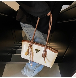 Détail d'un sac fourre-tout bicolore avec logo métallique et pompon sur les escaliers