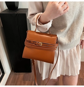 Détail d'un sac à main marron en cuir structuré avec ceinture décorative et boucle métallique