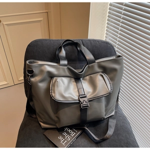 Détail d'un grand cabas gris foncé avec boucle tactique posé sur une chaise à rayures