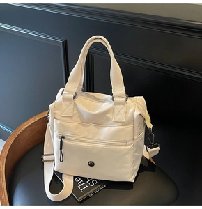 Detail of cream-white nylon tote bag with dual straps and round logo on textured chair