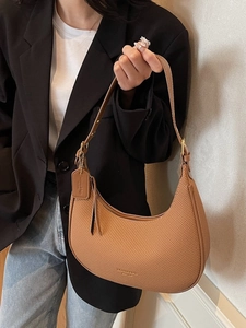 Brown woven crescent underarm bag with leather strap worn by a model in a black suit