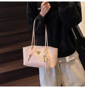 Détail du sac à bandoulière en cuir rose avec logo doré et pendentif décoratif à franges