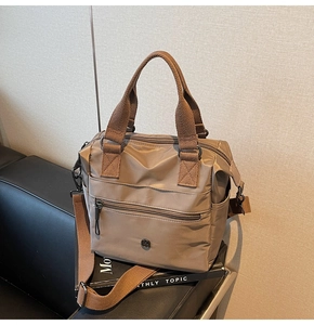 Detail of dark khaki nylon tote bag showing multiple zipper pockets on a leather chair