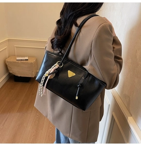 Détail du sac cabas noir avec logo triangle doré et foulard en soie sur l'épaule